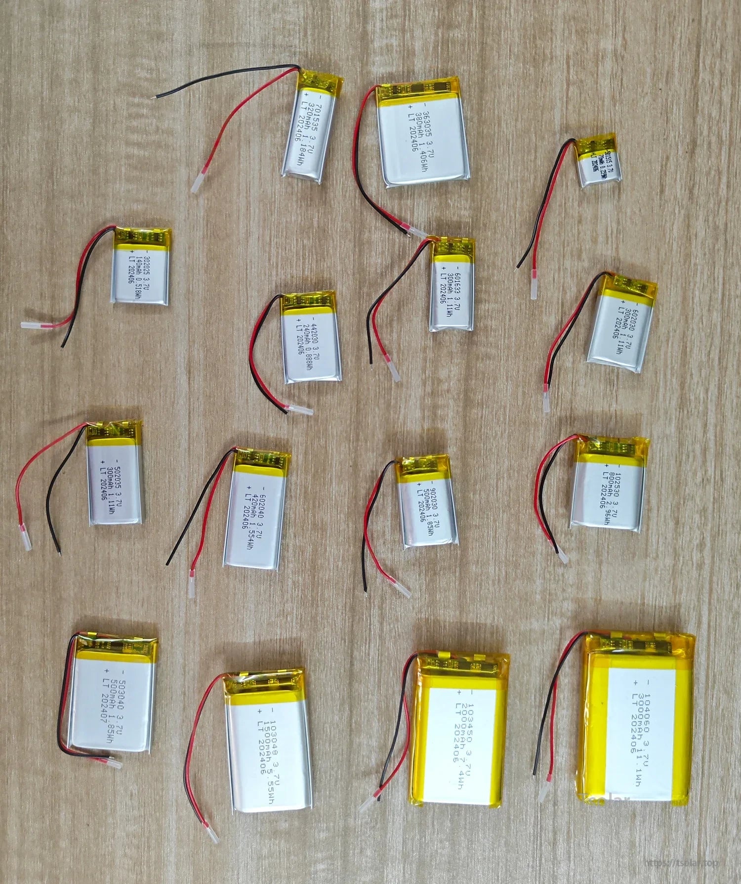 L7ADFJ 3.7V Lipo Battery, Various 3.7V Li-polymer batteries (11–4400mAh) in models 2025–10050, labeled with specs and color-coded wires, are neatly arranged on wood, showing size and capacity diversity.